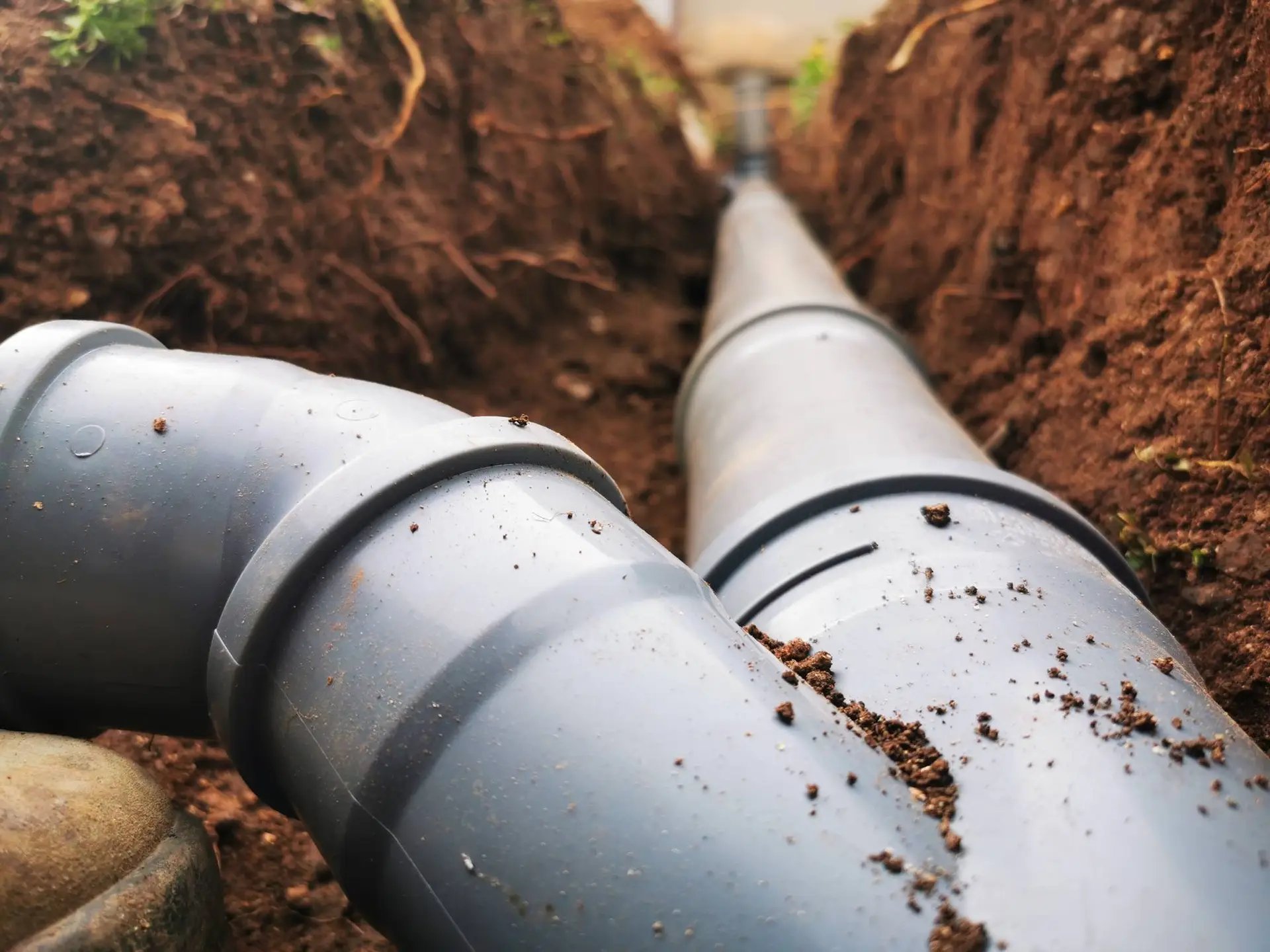 Close-up view of black plastic pipes being installed underground in a trench with brown soil, seen from a low angle—typical work for a plumber Bay Area, CA professionals rely on for quality installations.