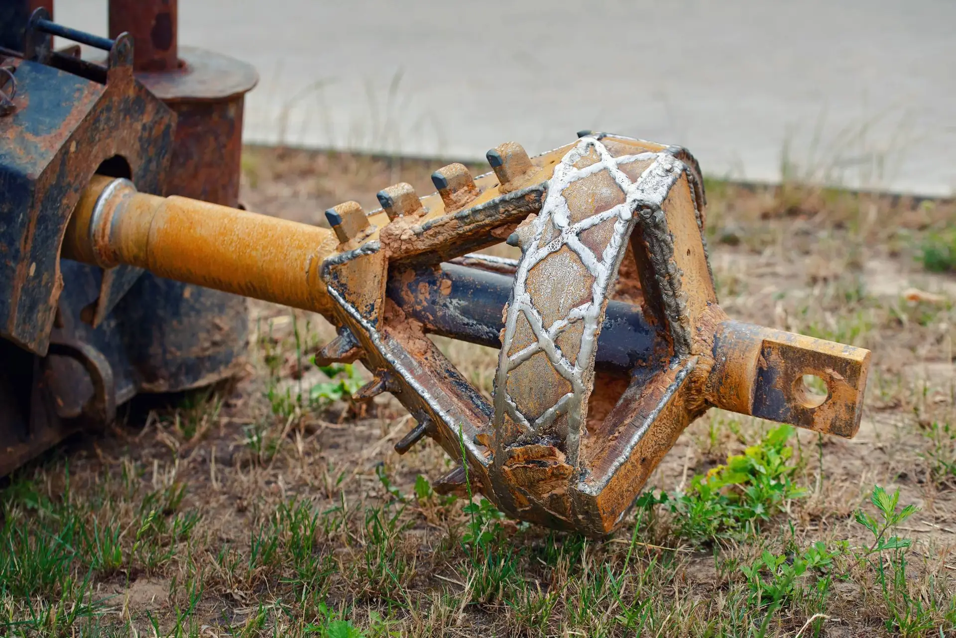 A close-up of a large, rusty horizontal directional drilling head lies on the ground, attached to a metal shaft—tools commonly used by a plumber Bay Area, CA—with grass and pavement in the background.